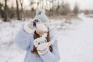 Smiling girl with unicorn Christmas decoration standing in snow - SSYF00067