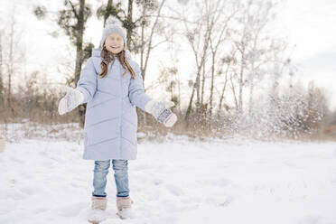 Fröhliches Mädchen mit Fäustlingen und Strickmütze spielt im Schnee - SSYF00068