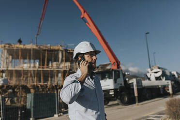 Mature man talking through smart phone at construction site - DMGF00974