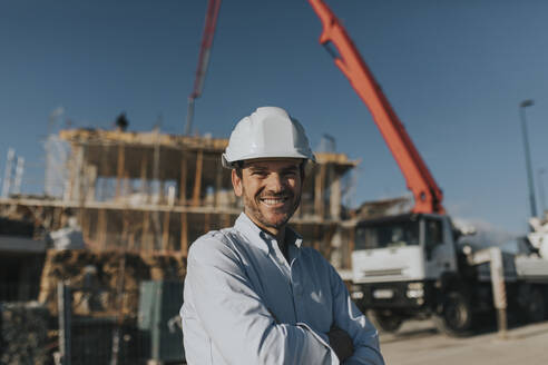 Glücklicher reifer Architekt mit Schutzhelm auf einer Baustelle - DMGF00976