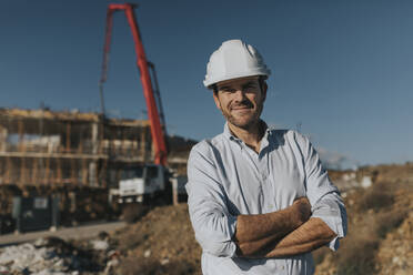 Smiling mature architect wearing hardhat standing at construction site - DMGF00979