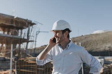 Happy mature architect talking on smart phone at construction site - DMGF00986