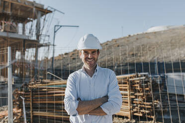 Happy mature architect with arms crossed in construction area - DMGF00987