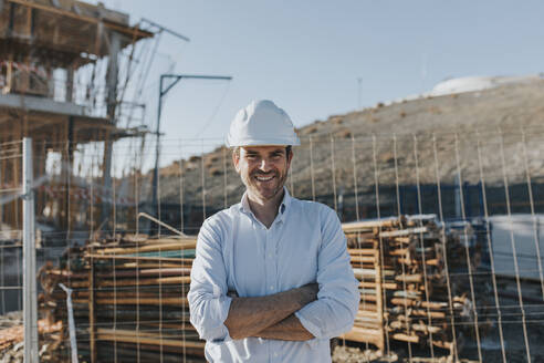 Glücklicher reifer Architekt mit verschränkten Armen auf einer Baustelle - DMGF00987