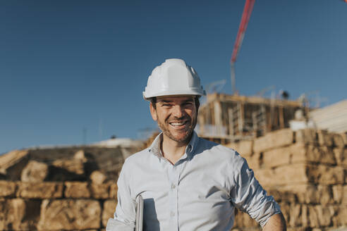 Glücklicher Architekt mit Schutzhelm auf einer Baustelle - DMGF00999