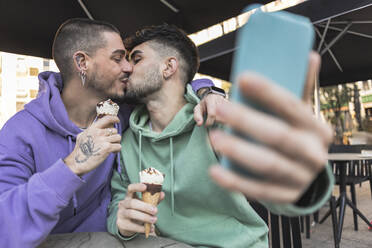 Ein schwules Paar küsst sich und macht ein Selfie mit dem Handy in einem Cafe - JCCMF09151