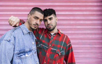 Young gay couple standing together in front of roller shutter wall - JCCMF09163