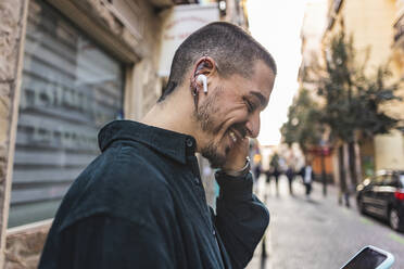 Smiling young man using smart phone on footpath - JCCMF09193