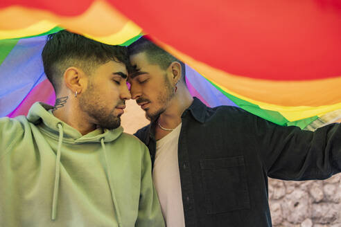 Gay couple with eyes closed under rainbow flag - JCCMF09215