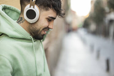 Lächelnder Mann mit Kopfhörern, der auf einem Fußweg Musik hört - JCCMF09241