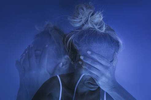 Depressed woman with head in hands against blue background - SIF00664