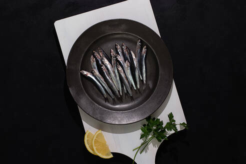 Top view of raw small fishes in plate on white board on black background - ADSF42890