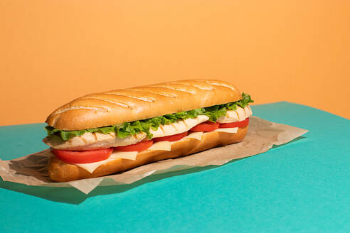 Von oben appetitlich Sandwich mit gegrilltem Huhn, frischem Salat und Tomaten auf Backpapier auf bunten Tisch Hintergrund serviert - ADSF42893