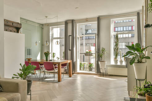 Esstisch mit Stühlen in einer modernen, hellen Wohnung, dekoriert mit Pflanzen, neben einem Sofa mit Kissen in einem stilvollen Wohnzimmer - ADSF42935