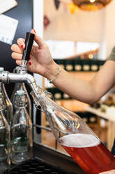 Anonyme Person gießt ein frisches Getränk in eine Glasflasche aus einer modernen Maschine in einem Geschäft - ADSF43001
