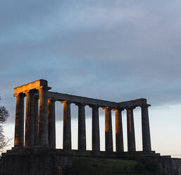 Von unten National Monument of Scotland mit Säulen in der Nähe blattlosen Baum gegen bewölkten blauen Himmel auf Calton Hill in der Tageszeit in Edinburgh, Schottland - ADSF43022