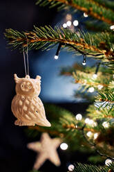 Christmas tree branches decorated with creative white owl and glowing lights in dark room - ADSF43049