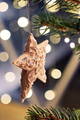 Star shaped white hanging on Christmas tree branch decorated with glowing garlands - ADSF43052