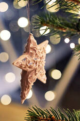 Sternförmiger weißer Behang an einem mit leuchtenden Girlanden geschmückten Weihnachtsbaumzweig - ADSF43052