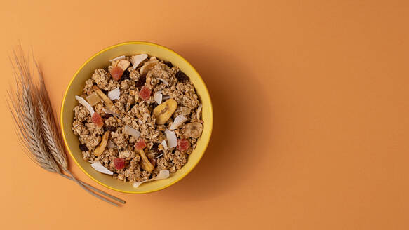 From above crispy granola with dried fruits in bowl on light table brown background - ADSF43058