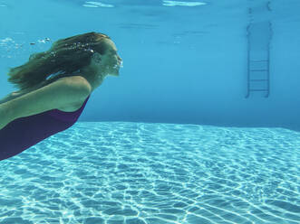 Adult woman diving in turquoise colored swimming pool - GWF07704