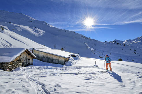 Österreich, Tirol, Sonnenschein über einer Skifahrerin, die eine einsame Hütte in den Tuxer Alpen passiert - ANSF00211