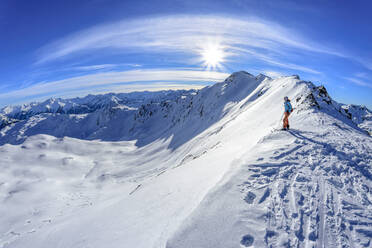 Österreich, Tirol, Sonne über einer Skifahrerin, die die schneebedeckte Landschaft in den Tuxer Alpen bewundert - ANSF00215