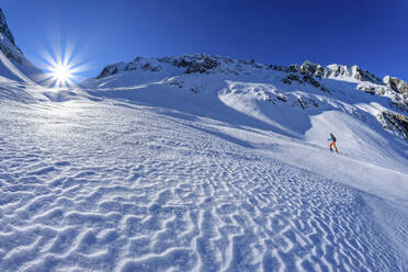 Österreich, Tirol, Skifahrerin beim Aufstieg auf die Piste in den Zillertaler Alpen mit Sonnenschein im Hintergrund - ANSF00216