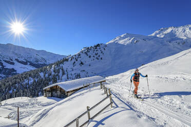 Österreich, Tirol, Sonne scheint über einer Skifahrerin, die an einer einsamen Hütte in den Tuxer Alpen vorbeikommt - ANSF00238