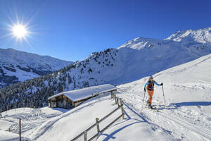 Österreich, Tirol, Sonne scheint über einer Skifahrerin, die an einer einsamen Hütte in den Tuxer Alpen vorbeikommt - ANSF00238