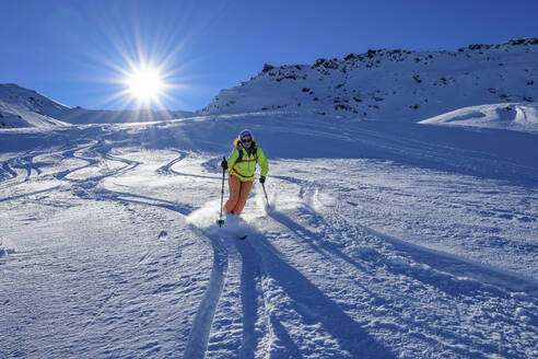 Österreich, Tirol, Sonnenschein über einer Skifahrerin, die einen schneebedeckten Hang in den Tuxer Alpen hinunterrutscht - ANSF00244