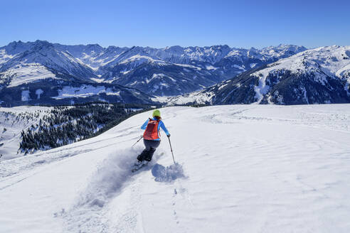 Austria, Tyrol, Female skier sliding down snowcapped slope in Kitzbuhel Alps - ANSF00259