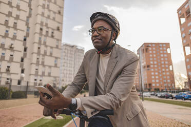 Thoughtful businessman with mobile phone and electric push scooter in city - JCCMF09252