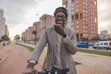 Happy mature businessman with helmet talking on speaker smart phone - JCCMF09254