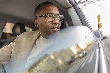 Mature businessman with eyeglasses looking out of car window - JCCMF09261