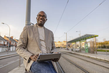 Lächelnder reifer Geschäftsmann mit Tablet-PC in der Straßenbahn - JCCMF09263