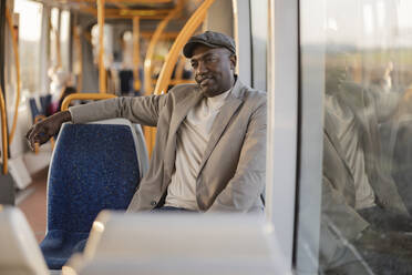 Geschäftsmann mit Schiebermütze, der auf einem Sitz in der Straßenbahn nachdenkt - JCCMF09271