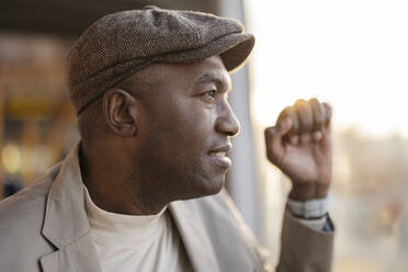 Contemplative commuter with flat cap looking through window at sunset - JCCMF09273