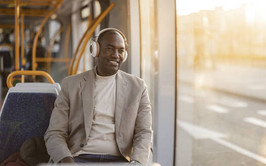 Lächelnder Geschäftsmann, der in einer Seilbahn über Kopfhörer Musik hört - JCCMF09275