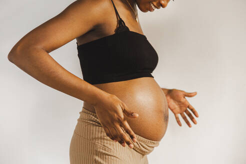 Frau mit schwangerem Bauch vor einer weißen Wand stehend - PCLF00237