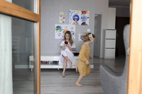 Mädchen spielt mit Schwester und benutzt Smartphone im Hintergrund - VIVF00345