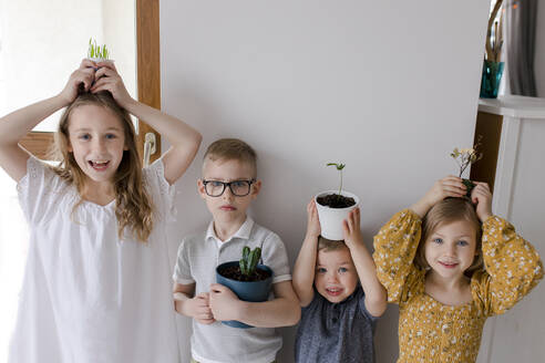 Siblings with houseplants on hands at home - VIVF00351