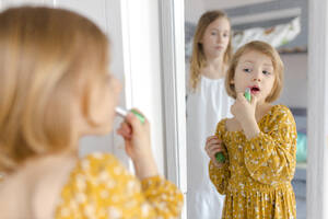 Mädchen trägt Lippenstift auf und schaut in den Spiegel zu Hause - VIVF00363
