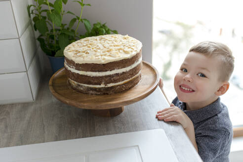 Glücklicher niedlicher Junge steht bei Kuchen in der Küche - VIVF00368