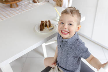 Glücklicher Junge mit Kuchen am Tisch sitzend - VIVF00378