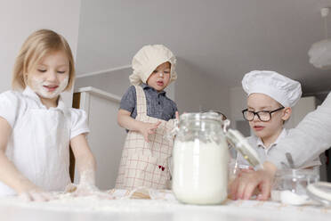 Siblings preparing dough with flour in kitchen - VIVF00398