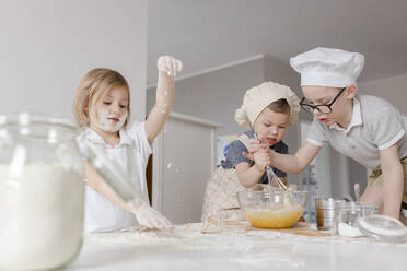 Girl preparing dough with brothers mixing eggs in bowl at home - VIVF00399