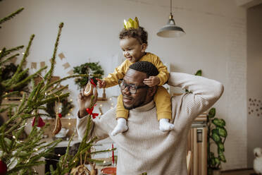 Happy man with daughter touching Christmas ornaments at home - MDOF00586