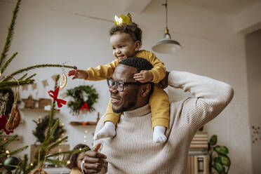 Smiling man with daughter touching Christmas ornaments at home - MDOF00587
