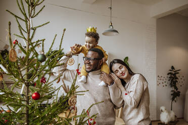 Happy father and mother with daughter touching Christmas ornament at home - MDOF00588